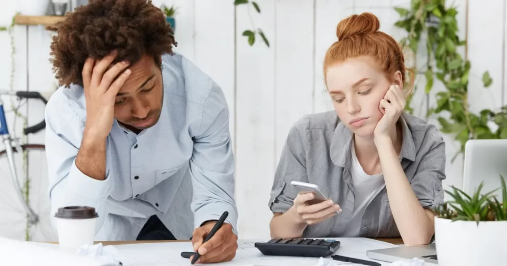 Casal jovem com expressão preocupada analisando contas e calculando dívidas, refletindo sobre estratégias de pagamento.