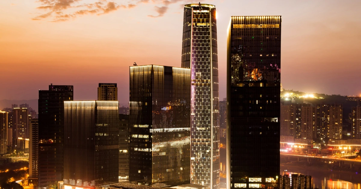 Vista panorâmica de uma cidade moderna com imponentes arranha-céus iluminados ao entardecer, refletindo o potencial de crescimento e valorização do mercado imobiliário.