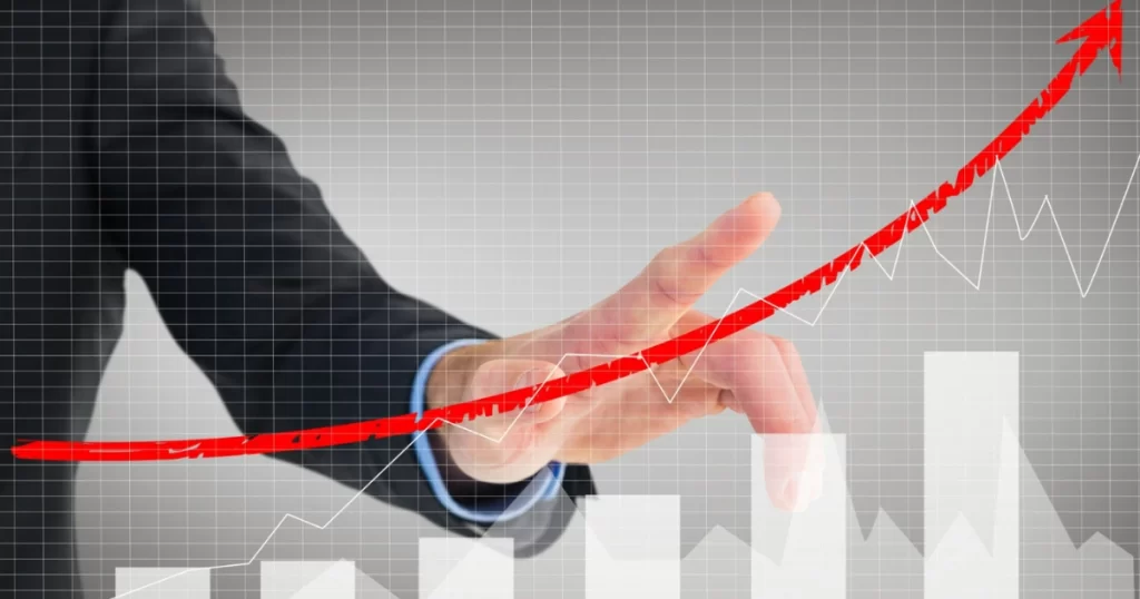 Mão de uma pessoa de terno apontando para um gráfico de tendência de alta em uma tela, simbolizando o crescimento dos investimentos.