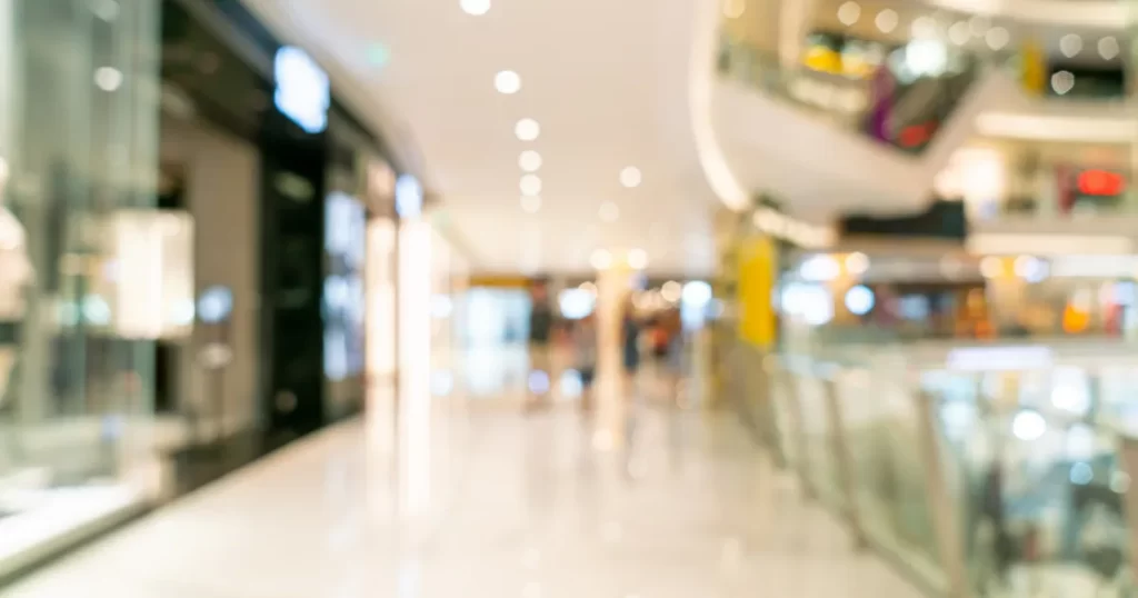 Imagem desfocada de um corredor de shopping center, com vitrines iluminadas e lojas de varejo, simbolizando a oportunidade de franquias em locais de alto tráfego.