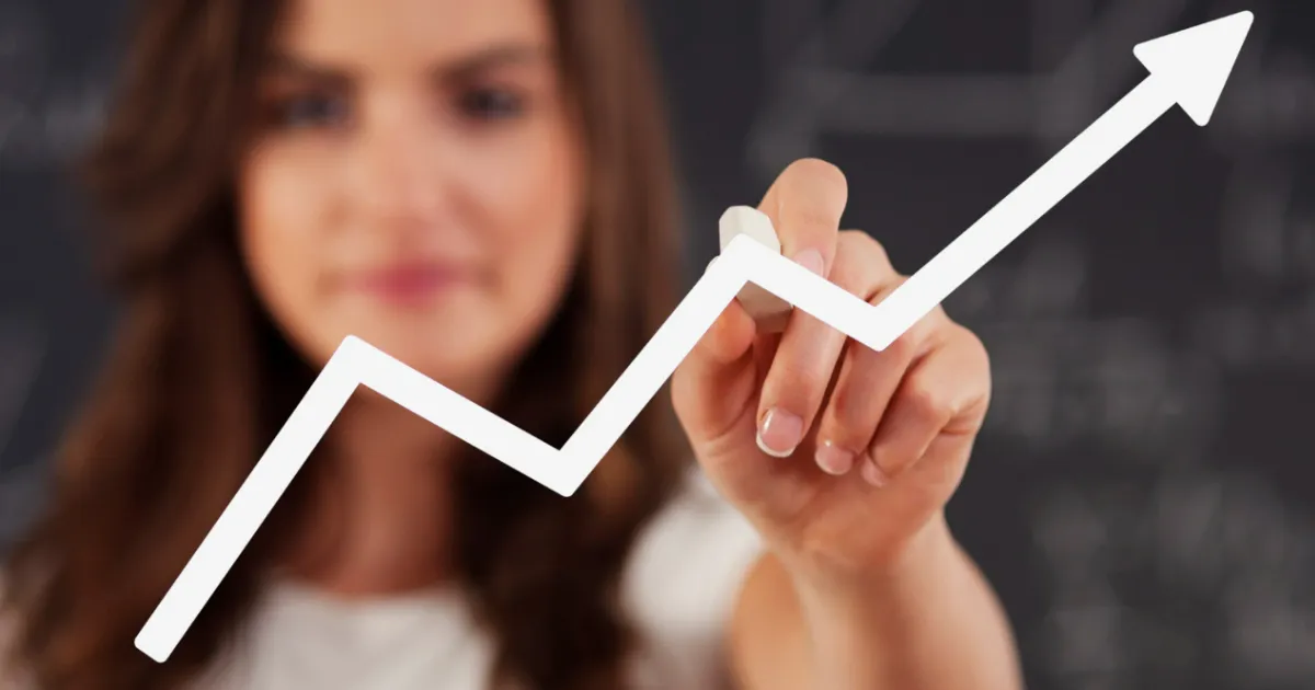 Mulher desenhando um gráfico de linha ascendente, simbolizando o crescimento do investimento e do patrimônio através de dividendos.