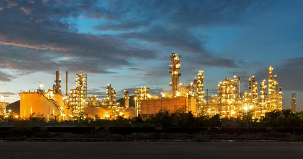Uma grande instalação industrial iluminada durante a noite, com várias torres e tubulações, representando a complexidade e o valor de uma empresa a ser avaliada através do valuation.