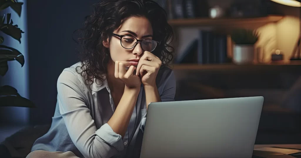 Jovem mulher de óculos olhando pensativamente para um laptop à noite, simbolizando a reflexão sobre as opções de diversificação de investimentos para sua faixa etária.