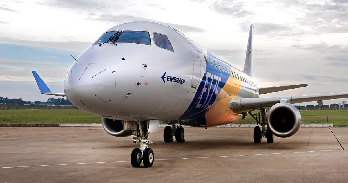 Avião Embraer branco com detalhes em amarelo e azul, parado em uma pista de aeroporto, simbolizando o sucesso e a presença da empresa no mercado global.