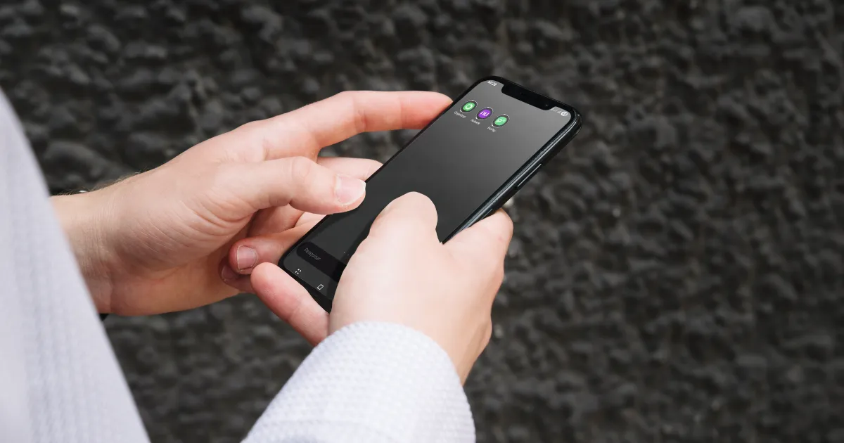 Uma pessoa segurando um smartphone que exibe a tela inicial com três ícones de aplicativos de finanças, simbolizando o uso da tecnologia para organizar a vida financeira.