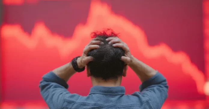 Investidor com as mãos na cabeça diante de um gráfico de ações em forte queda, representando os riscos e a volatilidade do mercado acionário.